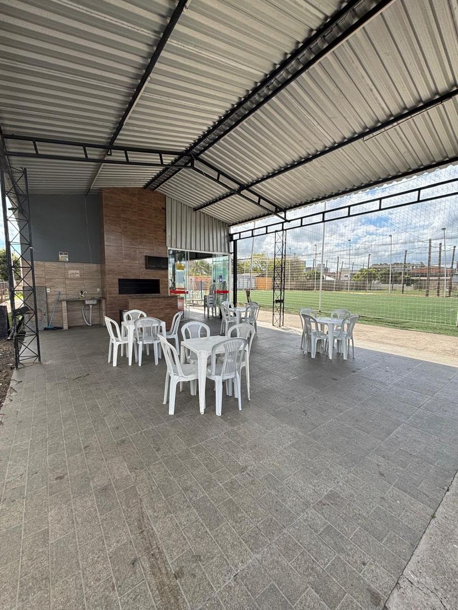 Espaço coberto da churrasqueira com mesas e vista para a quadra